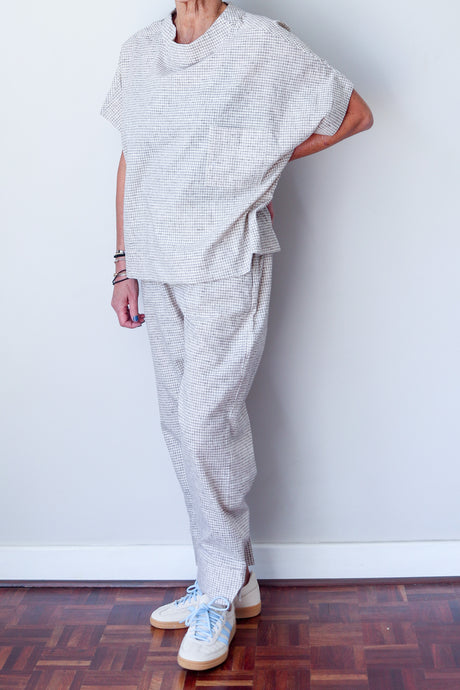 Person wearing a matching gray outfit with white sneakers against a white wall.